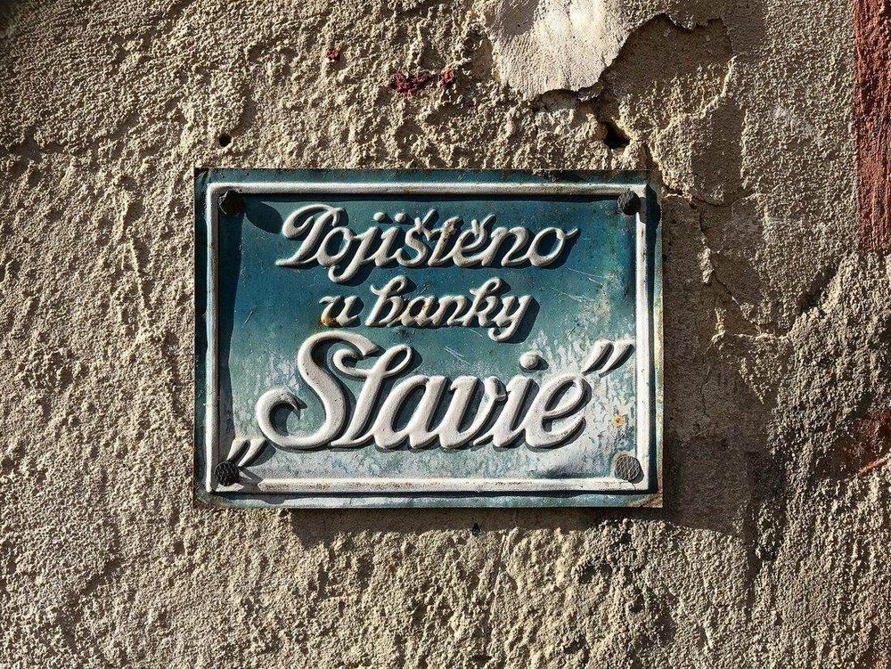 Emailová tabuľka s nápisom Pojištěno u banky Slavie na omietke pražského domu